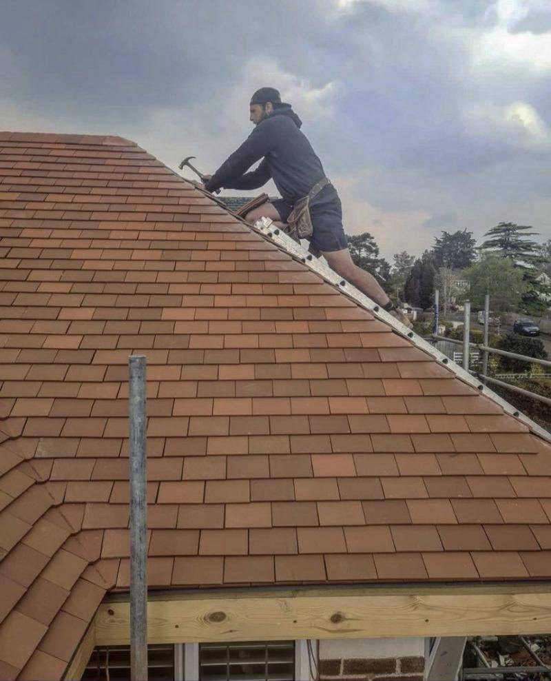 Modtra roofer carefully laying plain clay tiles on a pitched roof