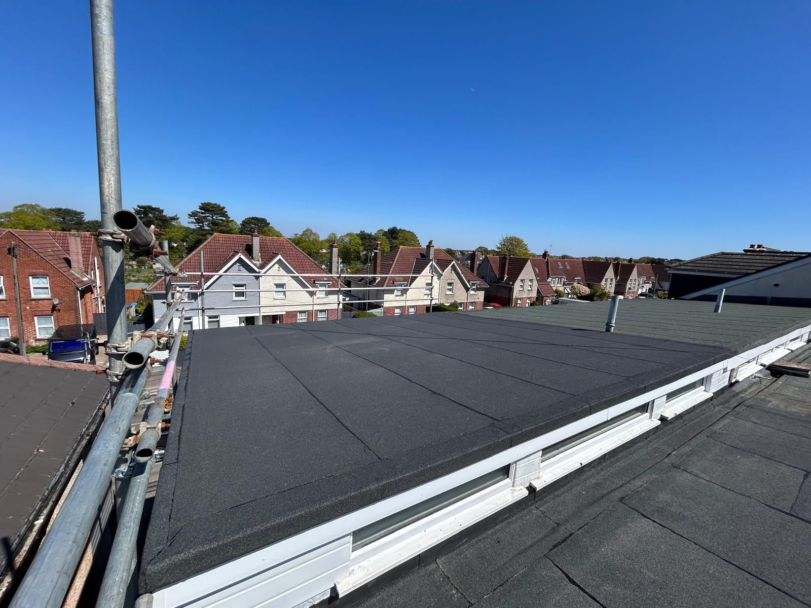 Completed torch-on felt flat roof with a dark mineral cap sheet, neat sheet joints and new edge trims above white guttering