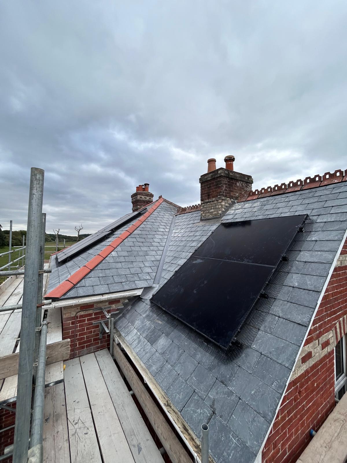 Natural slate re-roof with solar panels edged in bird mesh, a lead valley, brick chimneys and decorative red clay ridge tiles