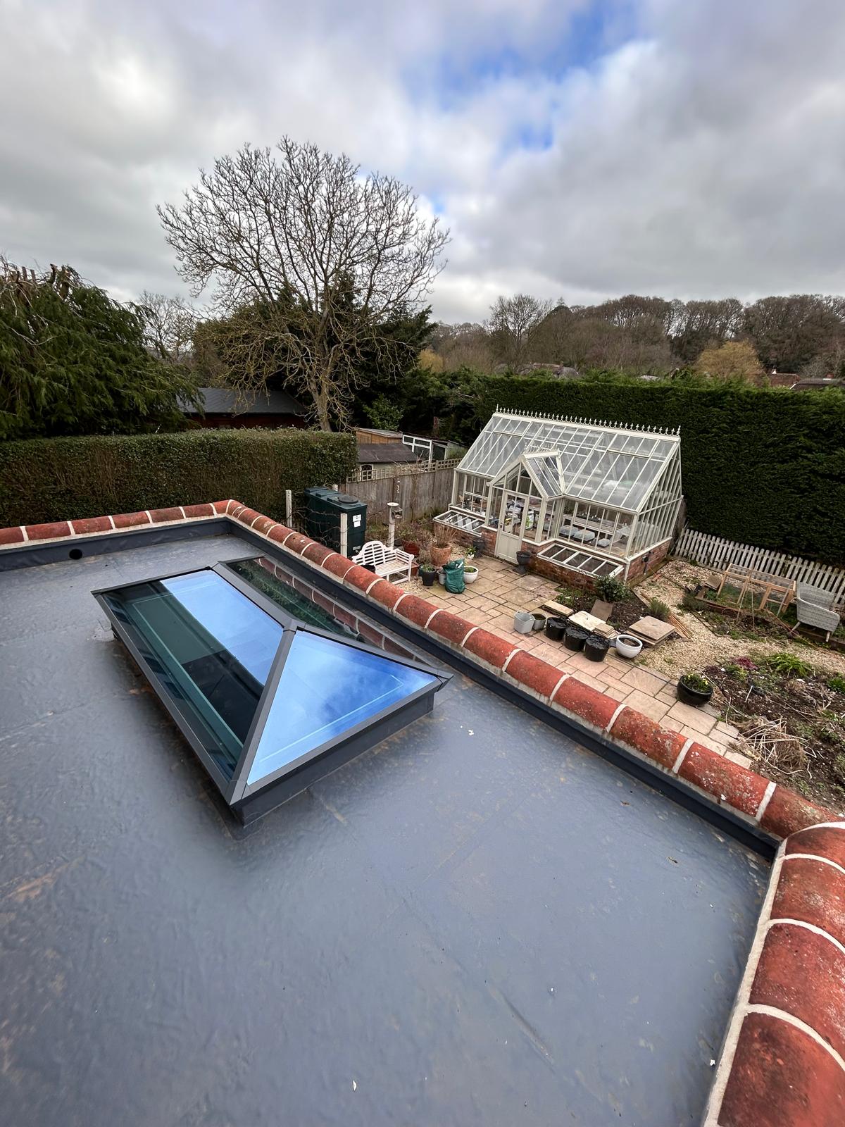 Grey membrane flat roof with a glazed roof lantern and rounded red clay coping along the parapet
