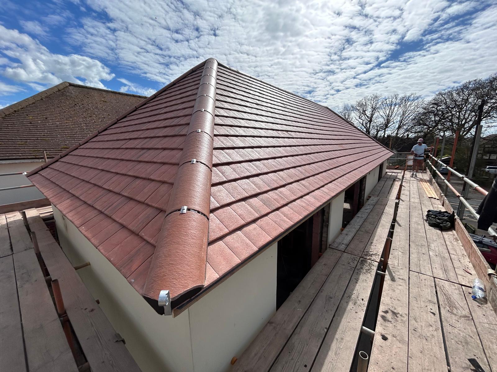 New hipped extension roof covered in red concrete plain tiles with mechanically fixed hip tiles, viewed from scaffolding