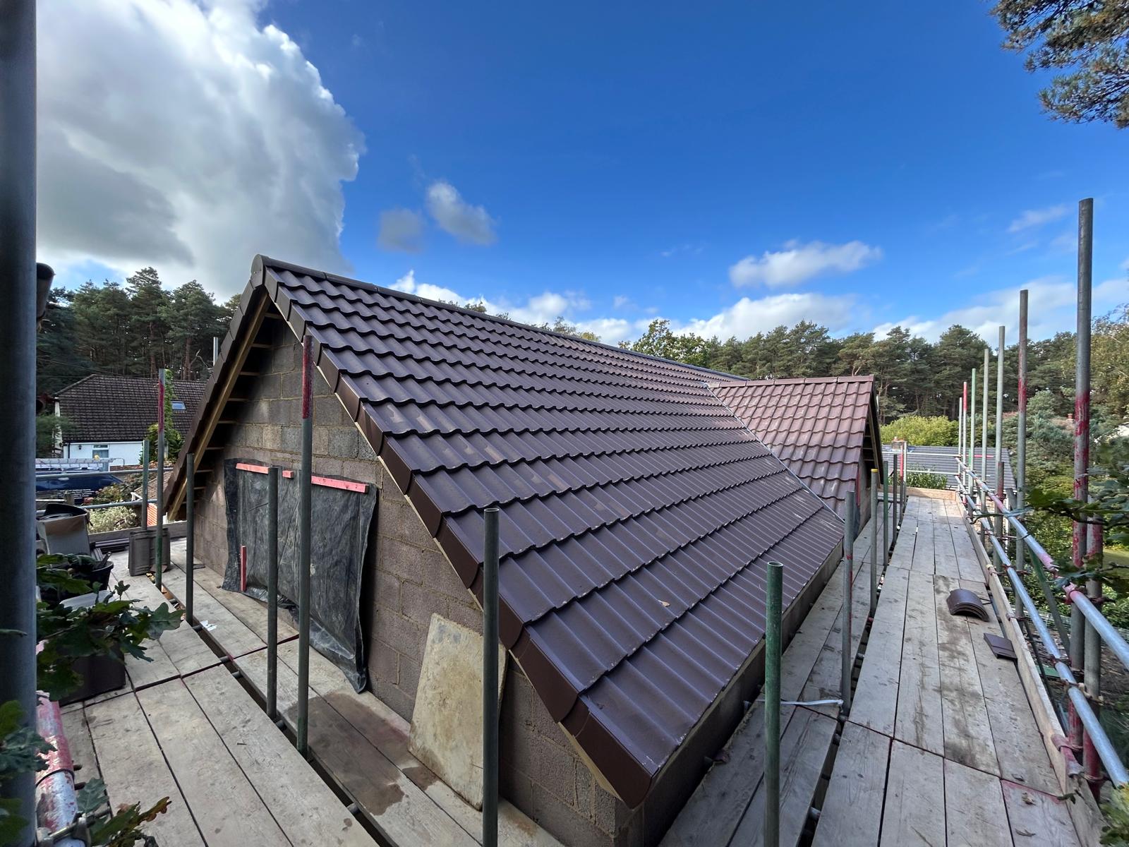 New-build gable roof covered in brown interlocking concrete tiles with a dry verge along the gable edges, viewed from scaffolding
