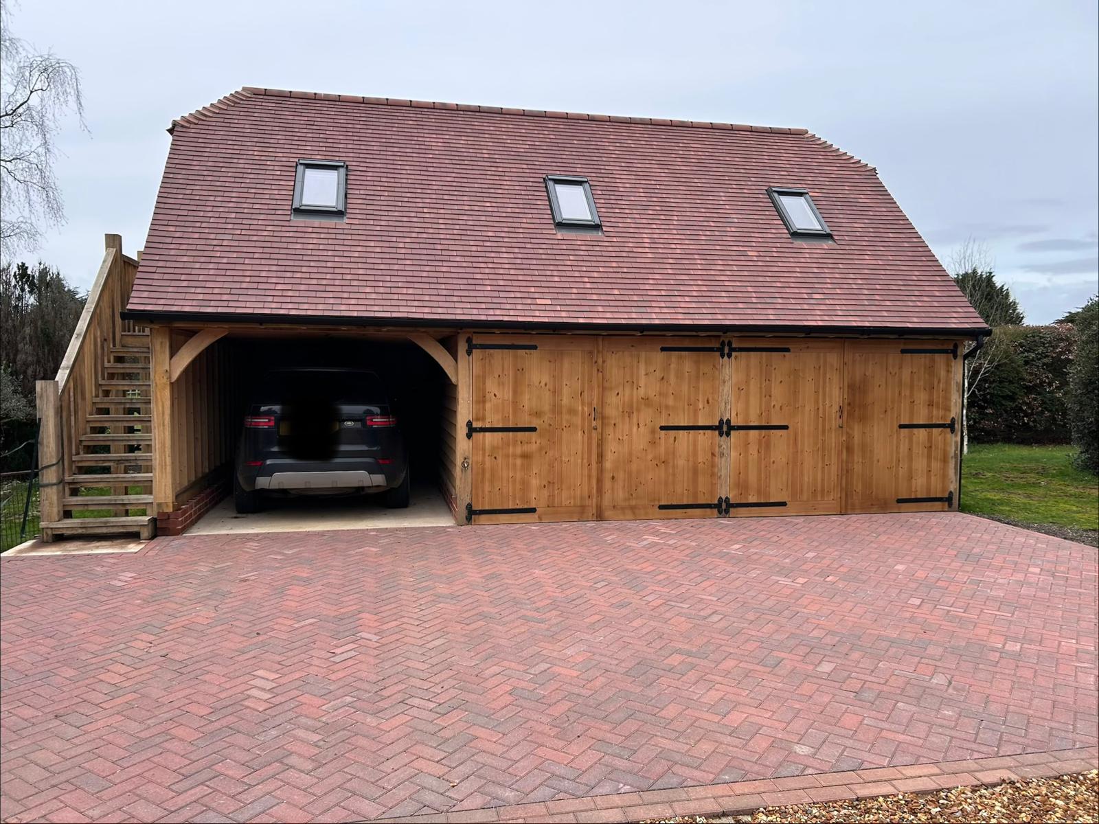 Front of an oak-frame garage with a plain clay tile roof and three Velux roof windows above the timber doors